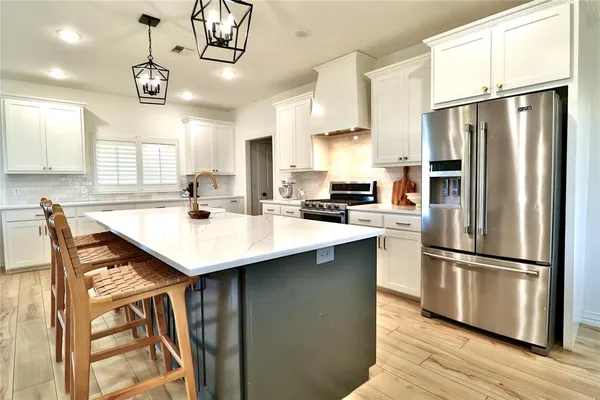 a kitchen with stainless steel appliances a sink a refrigerator a stove a kitchen island with wooden floor and cabinets