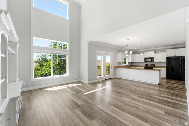 1614 Aspen Loop Provo, UT 84606 - Photo 10 of 47 Great room featuring soaring ceilings, expansive windows, wood-finish flooring, a built-in display cabinet, and an open-concept kitchen with white cabinetry and stainless steel appliances