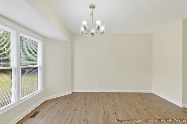 an empty room with wooden floor chandelier fan and windows