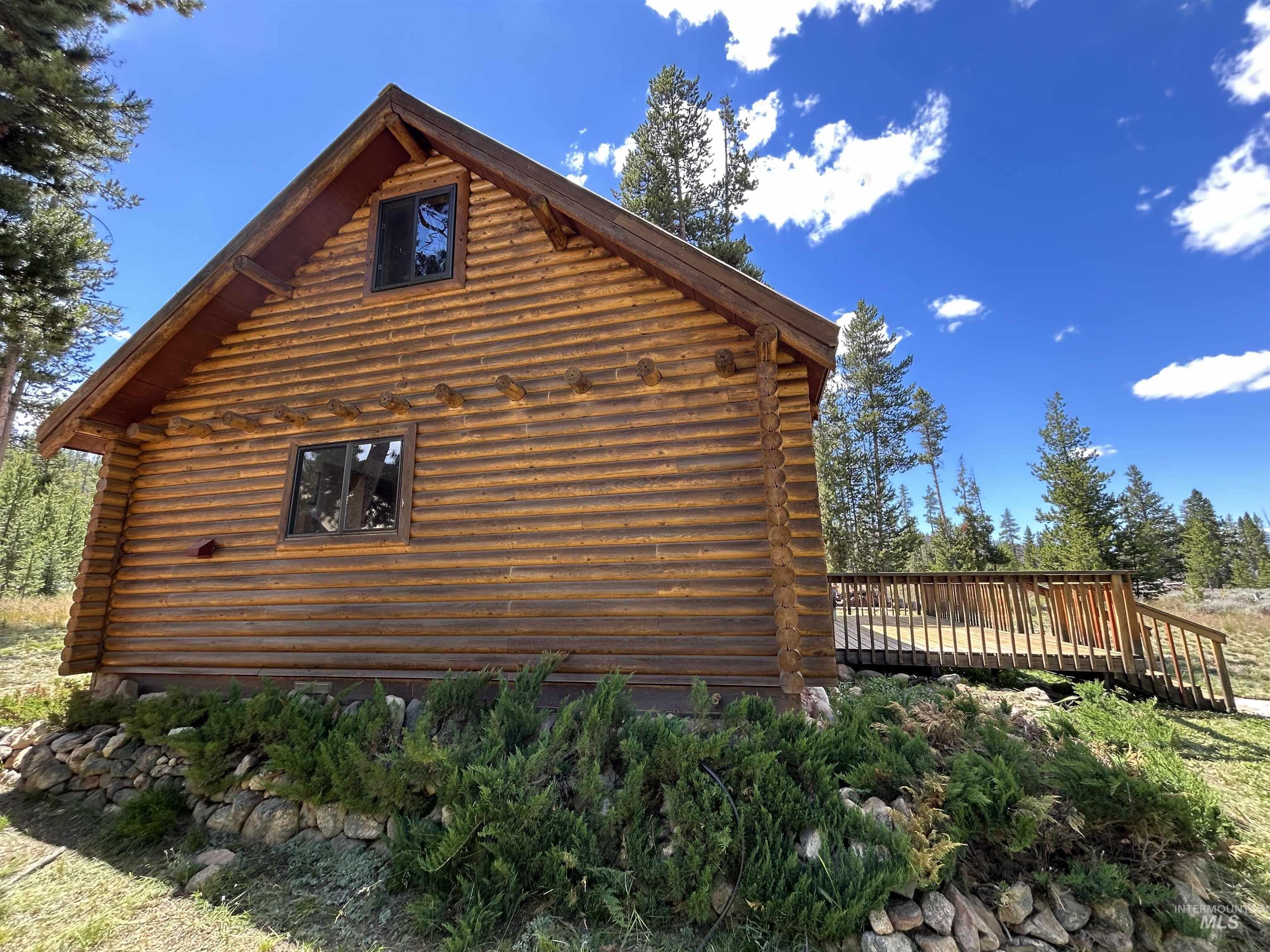 35 Sawtooth Way Stanley, ID 83278 - Photo 9 of 36 Log cabin exterior featuring a gable roof, two windows, and a raised wooden deck with railings