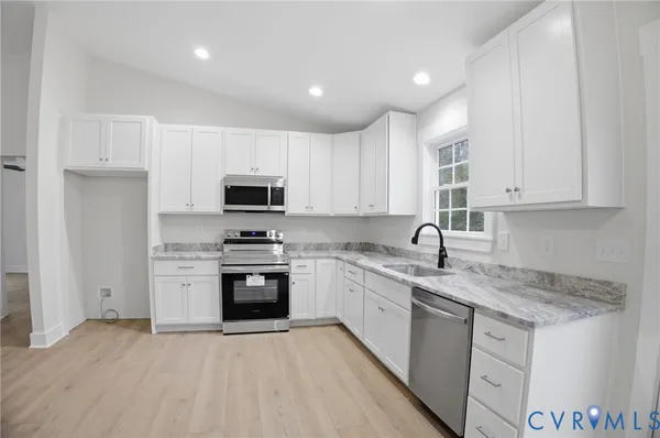 a large kitchen with granite countertop a stove top oven a sink dishwasher and a refrigerator with wooden floor