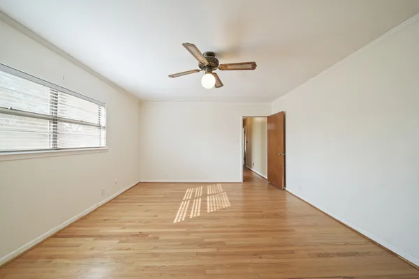 an empty room with wooden floor ceiling fan and windows