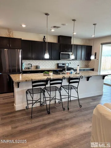 a kitchen with stainless steel appliances kitchen island granite countertop a stove top oven a sink a dining table and chairs with wooden floor