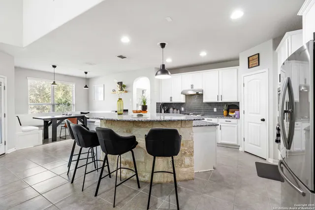 a kitchen with stainless steel appliances granite countertop a refrigerator a sink dishwasher a dining table and chairs with wooden floor