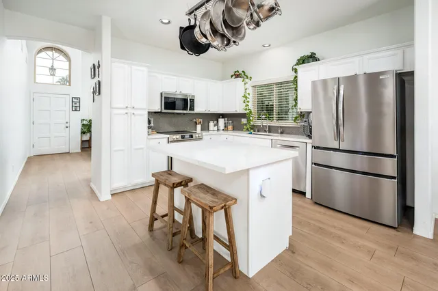 a kitchen with stainless steel appliances a refrigerator a sink dishwasher a stove and white cabinets with wooden floor