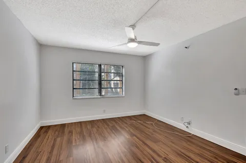 an empty room with wooden floor chandelier fan and windows
