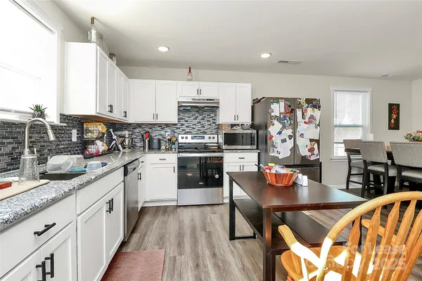 a kitchen with stainless steel appliances granite countertop a stove top oven a sink dishwasher and white cabinets with wooden floor