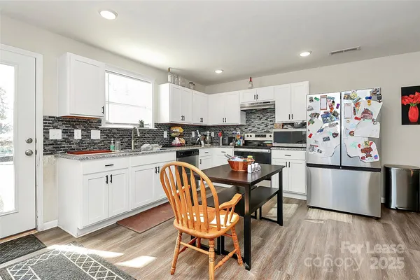 a kitchen with stainless steel appliances granite countertop a stove a sink dishwasher and a refrigerator with white cabinets
