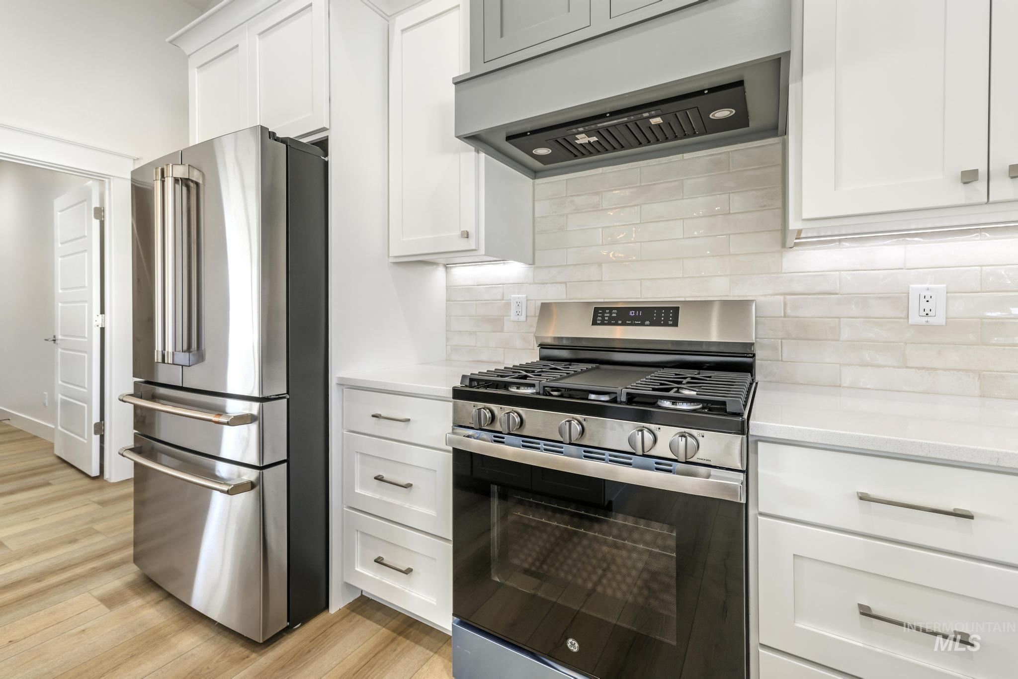1428 Haizlee Way Twin Falls, ID 83301 - Photo 5 of 23 Kitchen with stainless steel appliances, ventilation hood, white cabinets, light wood-type flooring, and light stone countertops
