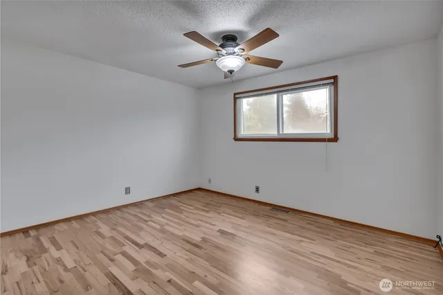 a view of an empty room with wooden floor and a ceiling fan