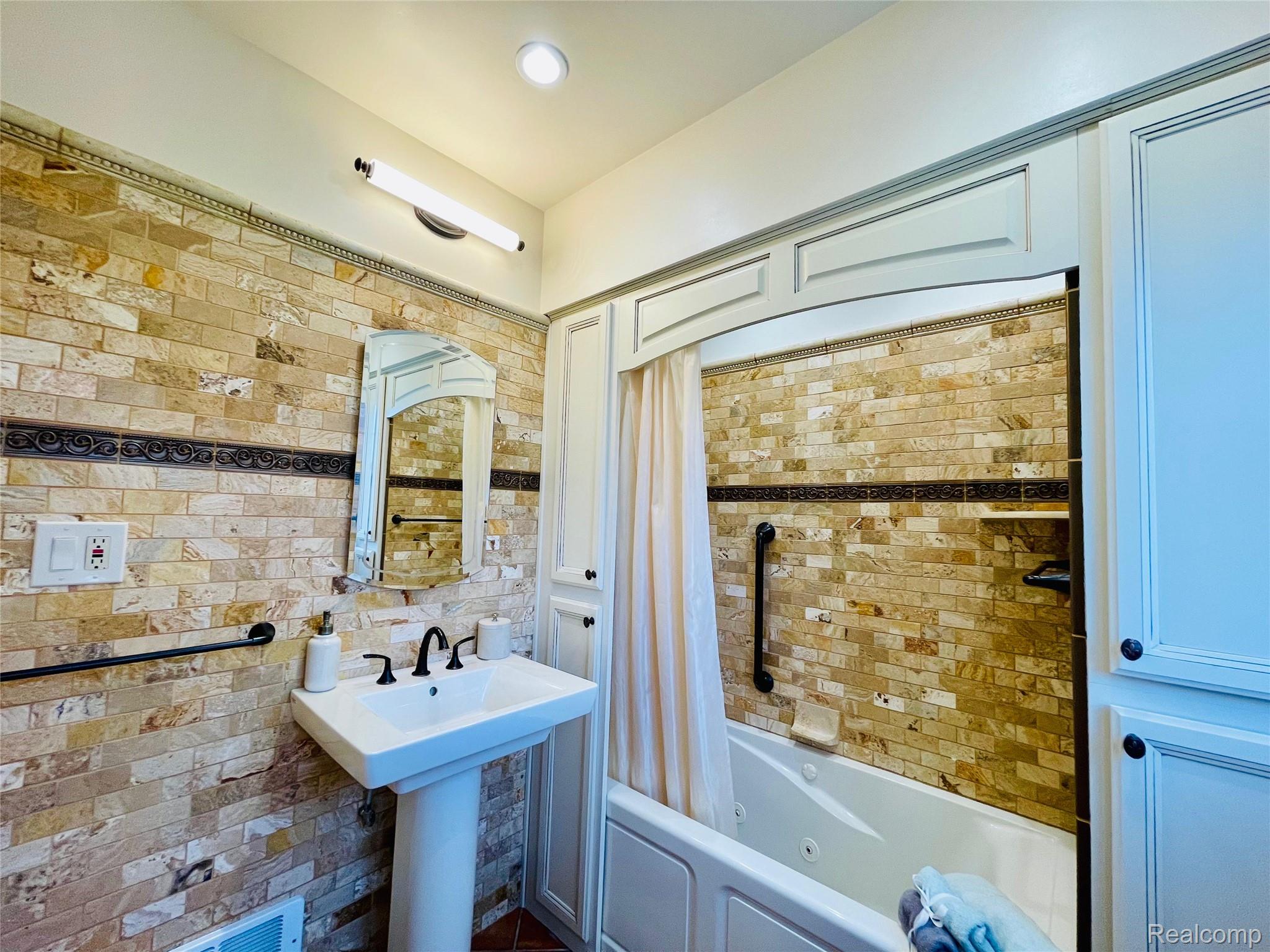 60 Devon Road Bloomfield Hills, MI 48302 - Photo 27 of 50 Bathroom featuring floor-to-ceiling stone tile walls, a pedestal sink with a matte black faucet, and a jetted bathtub