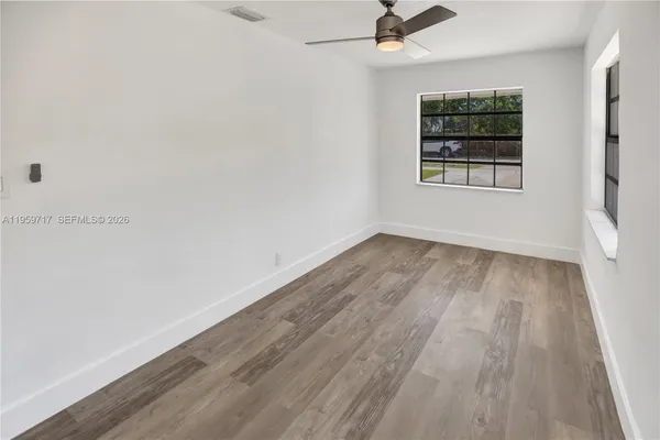 an empty room with wooden floor chandelier fan and windows
