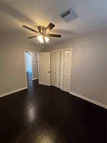 a view of an empty room with wooden floor and a ceiling fan