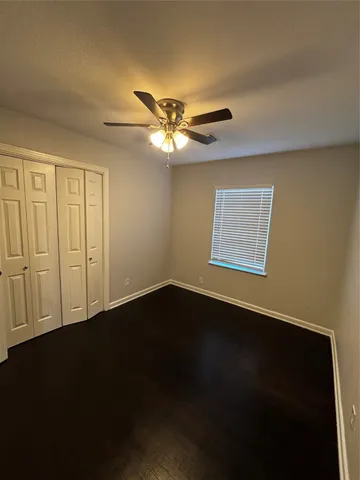 a view of an empty room with wooden floor and a ceiling fan