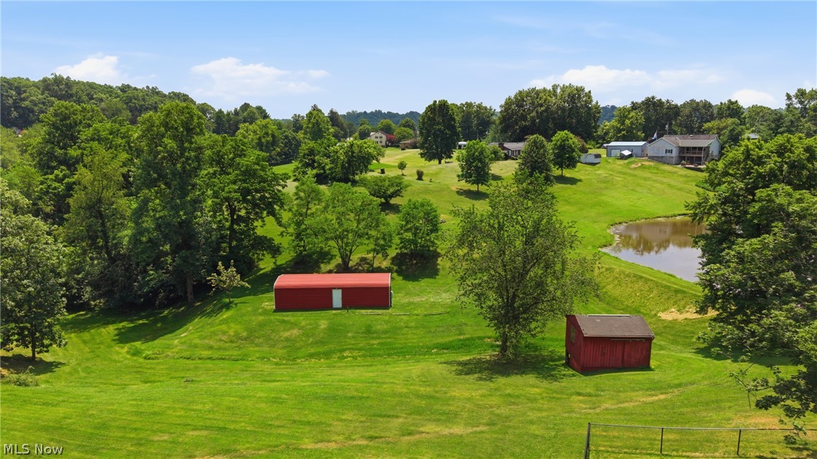 89 Dagg Road Parkersburg, WV 26101 - Photo 42 of 45 Expansive green lawn with mature trees, a red storage shed, a red barn, and a visible pond