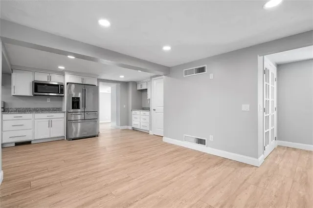 a view of an empty room and kitchen with wooden floor