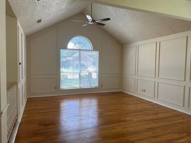 an empty room with wooden floor fan and windows