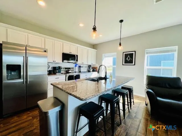 a kitchen with stainless steel appliances granite countertop a refrigerator a stove a sink a dining table and chairs with wooden floor