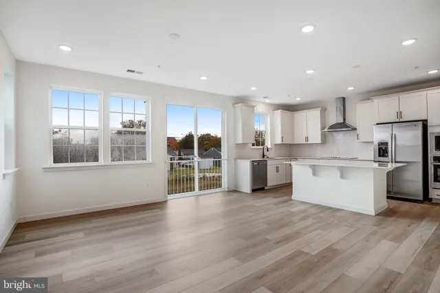 a large kitchen with stainless steel appliances granite countertop a stove a sink a refrigerator and white cabinets with wooden floor