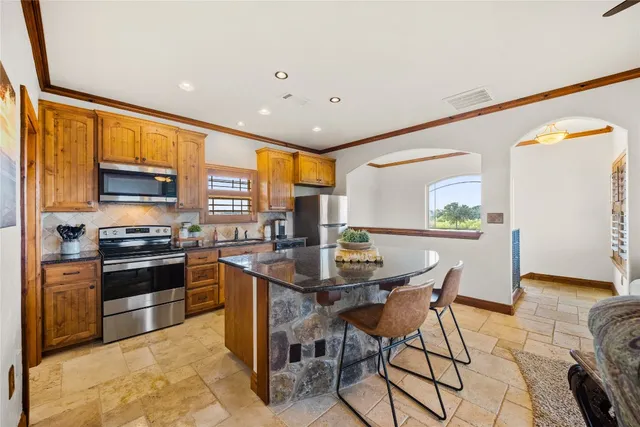 a kitchen with stainless steel appliances kitchen island granite countertop a stove top oven a sink a dining table and chairs with wooden floor