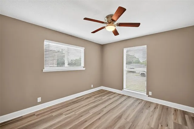 an empty room with wooden floor fan and windows