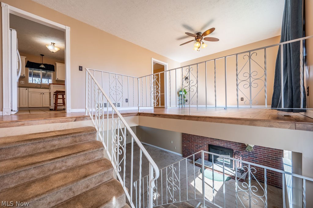 3601 River Road Vienna, WV 26105 - Photo 5 of 40 Staircase featuring a ceiling fan, a textured ceiling, and a brick fireplace