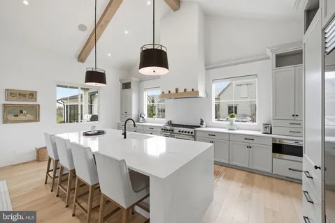 a large white kitchen with a stove a sink dishwasher and a dining table with wooden floor
