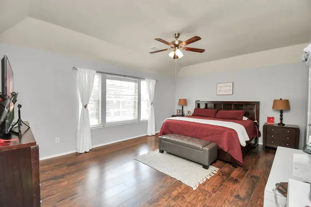 a spacious bedroom with a bed a dresser and wooden floor
