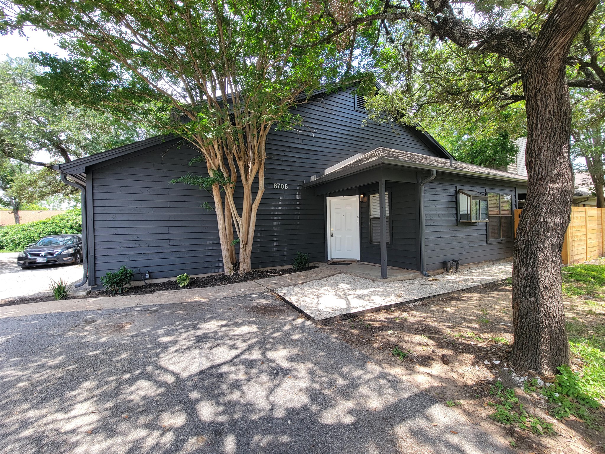 8706 Schick Road, Unit A Austin, TX 78729 - Photo 6 of 33 A dark-toned dwelling featuring horizontal siding and a covered front entry, nestled among mature trees.