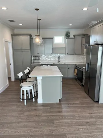 a kitchen with stainless steel appliances granite countertop a sink a stove a refrigerator and island with wooden floor