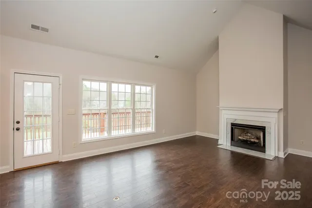 an empty room with wooden floor fireplace and windows
