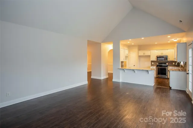 a view of an empty room with wooden floor and a kitchen