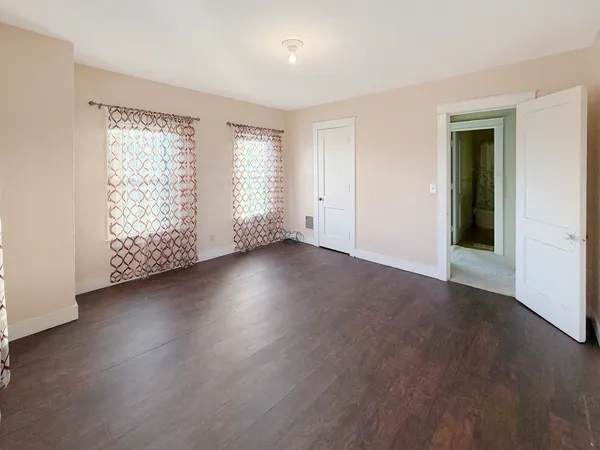 an empty room with wooden floor and windows with curtains
