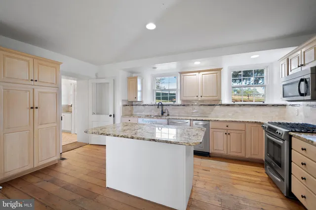 a kitchen with stainless steel appliances granite countertop a sink a stove a refrigerator and island with wooden floor