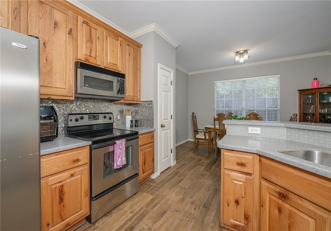 1425 West Villa Maria Road, Unit 103 Bryan, TX 77801 - Photo 9 of 30 Kitchen featuring stainless steel appliances, crown molding, dark wood-style flooring, backsplash, and light stone counters