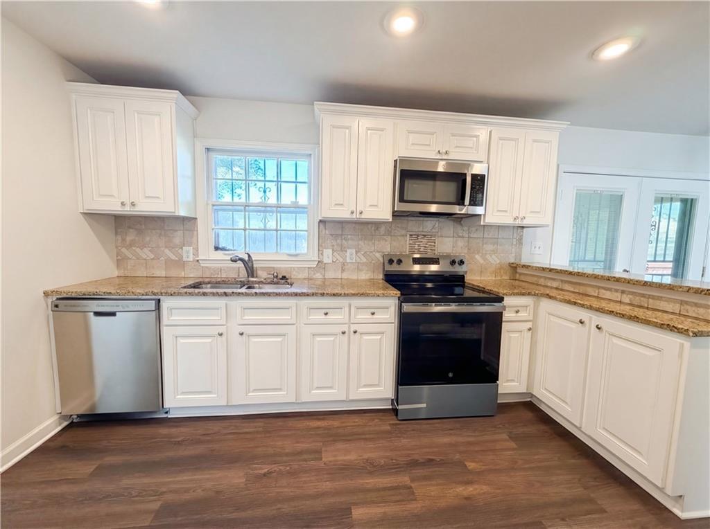4055 Tecumseh Trail Conley, GA 30288 - Photo 10 of 30 a kitchen with granite countertop white cabinets a sink a stove a microwave and wooden floors