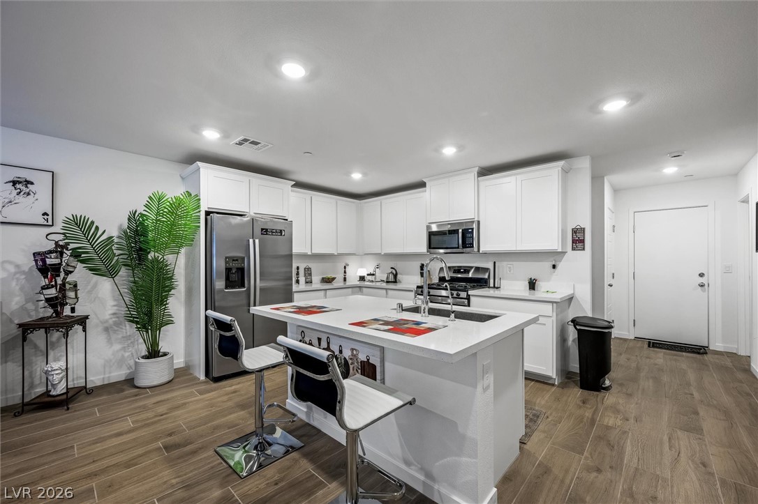 175 Hazel Heights Henderson, NV 89011 - Photo 11 of 55 Kitchen featuring white cabinetry, stainless steel appliances, wood tiled floors, a center island with sink, and a kitchen bar