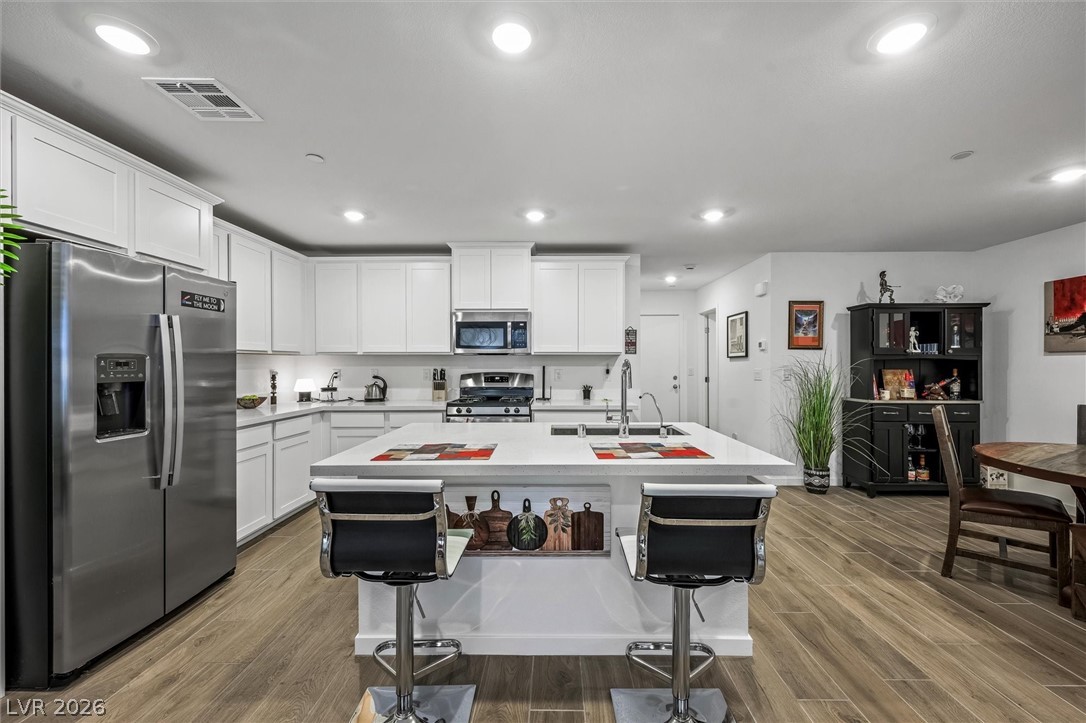 175 Hazel Heights Henderson, NV 89011 - Photo 12 of 55 Kitchen featuring stainless steel appliances, wood finished floors, white cabinetry, a center island with sink, and recessed lighting