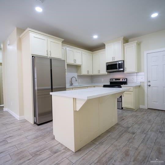 3052 Briggs Road, Unit C Weslaco, TX 78596 - Photo 6 of 16 Kitchen featuring wood-finish flooring, an island with a light-colored countertop, cream cabinetry, stainless steel appliances, and recessed lighting