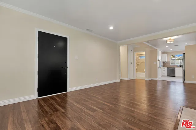 a view of an empty room with wooden floor and a kitchen