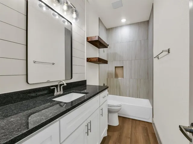 a bathroom with a granite countertop sink a toilet a mirror and shower