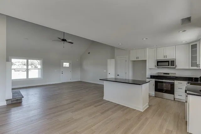 a kitchen with stainless steel appliances granite countertop a stove top oven a sink and white cabinets with wooden floor