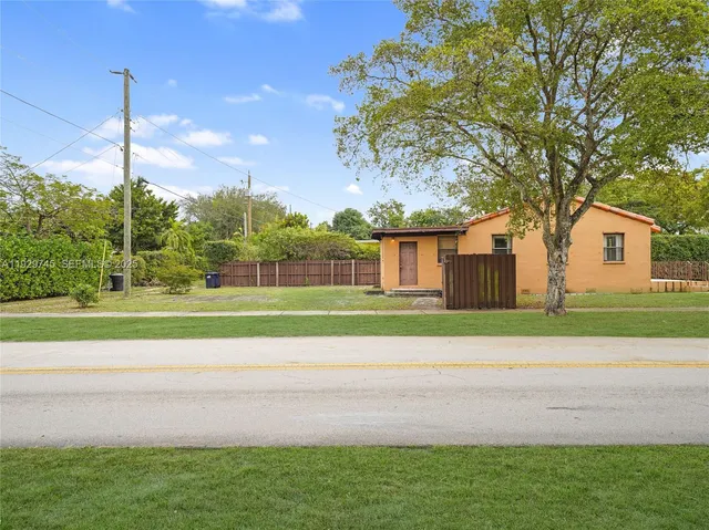 a small white house with a yard and palm trees