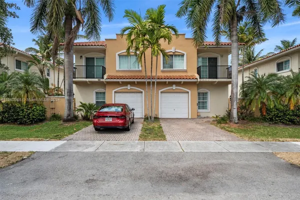 a yellow house with a small yard and palm trees