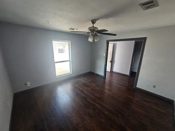 an empty room with wooden floor chandelier fan and windows