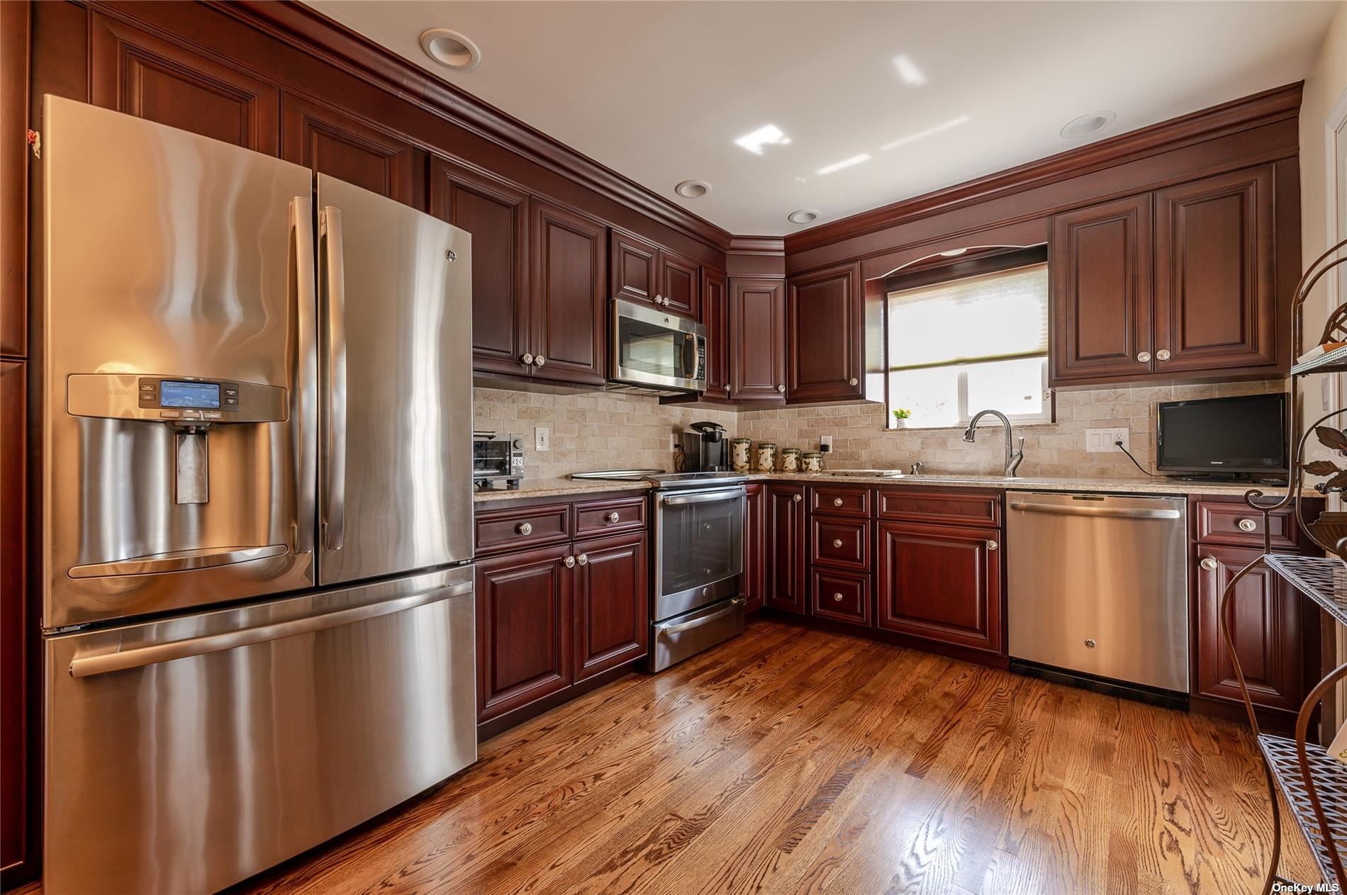 a kitchen with granite countertop wooden floors stainless steel appliances a sink and a window