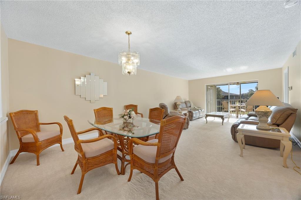 5683 Rattlesnake Hammock Road, Unit A202 Naples, FL 34113 - Photo 6 of 27 Dining room featuring carpet, a textured ceiling, and a chandelier