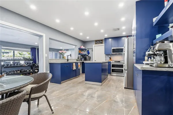 a living room with stainless steel appliances kitchen island granite countertop a table chairs in it and a wooden cabinets