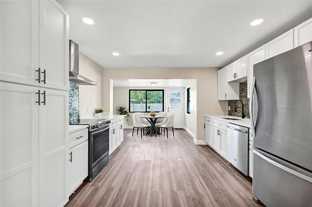 a kitchen with granite countertop stainless steel appliances a stove refrigerator a sink dishwasher a dining table and chairs with wooden floor