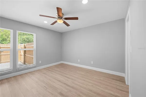 an empty room with wooden floor fan and windows